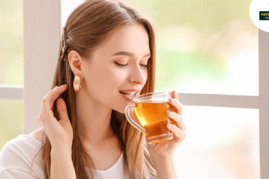 A woman sips tea peacefully in front of a window for glowing skin, surrounded by soft light and a tranquil setting.