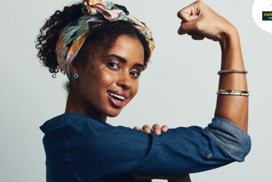 A woman displays a powerful stance with her fist raised high, adorned with a headband on her arm, embodying empowerment.
