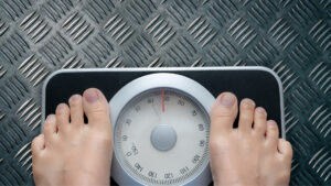 A person stands on a scale, their feet positioned on the top, indicating a moment of weighing themselves.