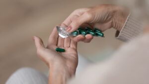  A woman holds a green pill in her hand, contemplating its significance with a focused expression.
