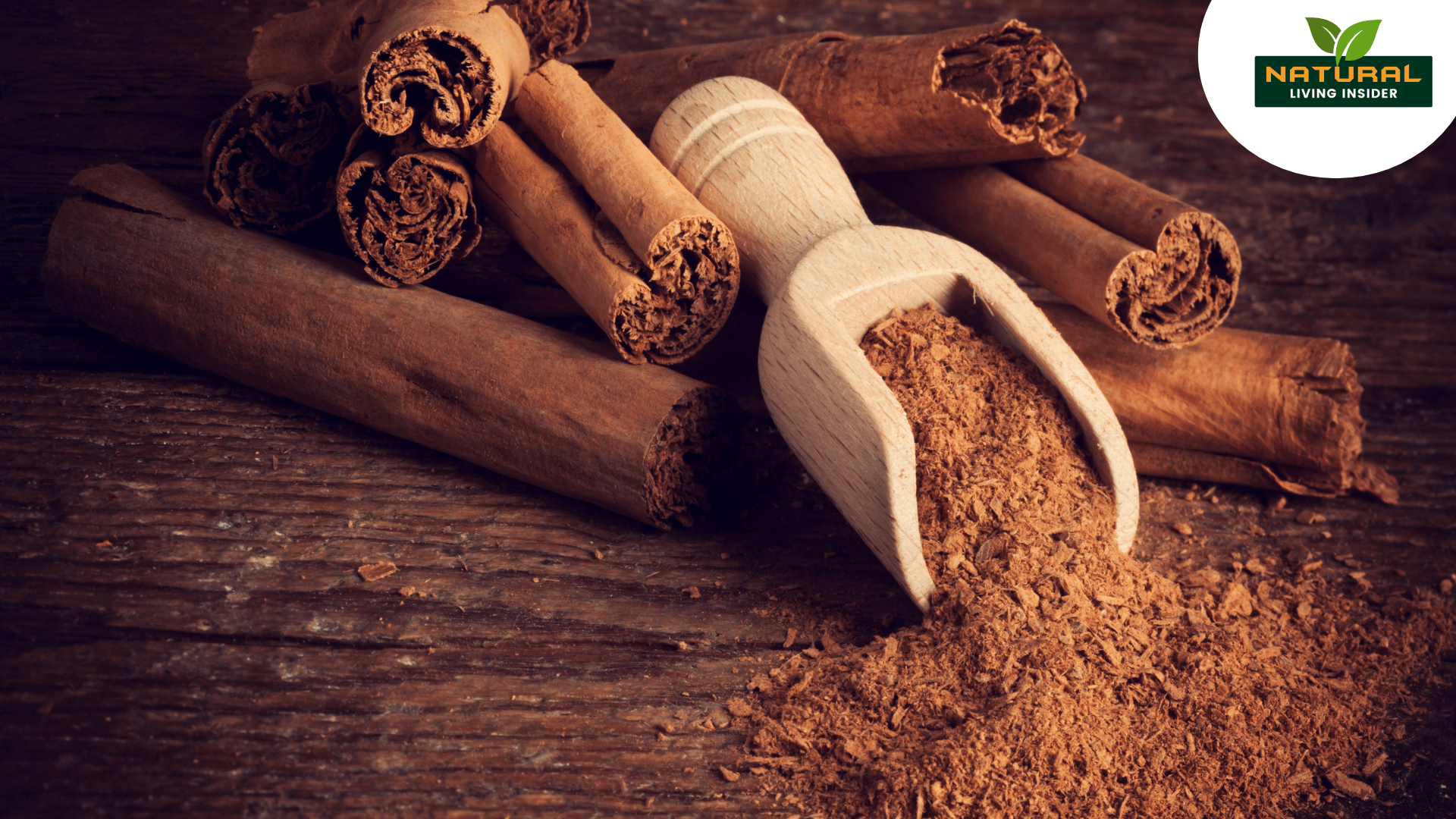 A wooden scoop filled with ground cinnamon rests beside several cinnamon sticks on a rustic wooden surface.
