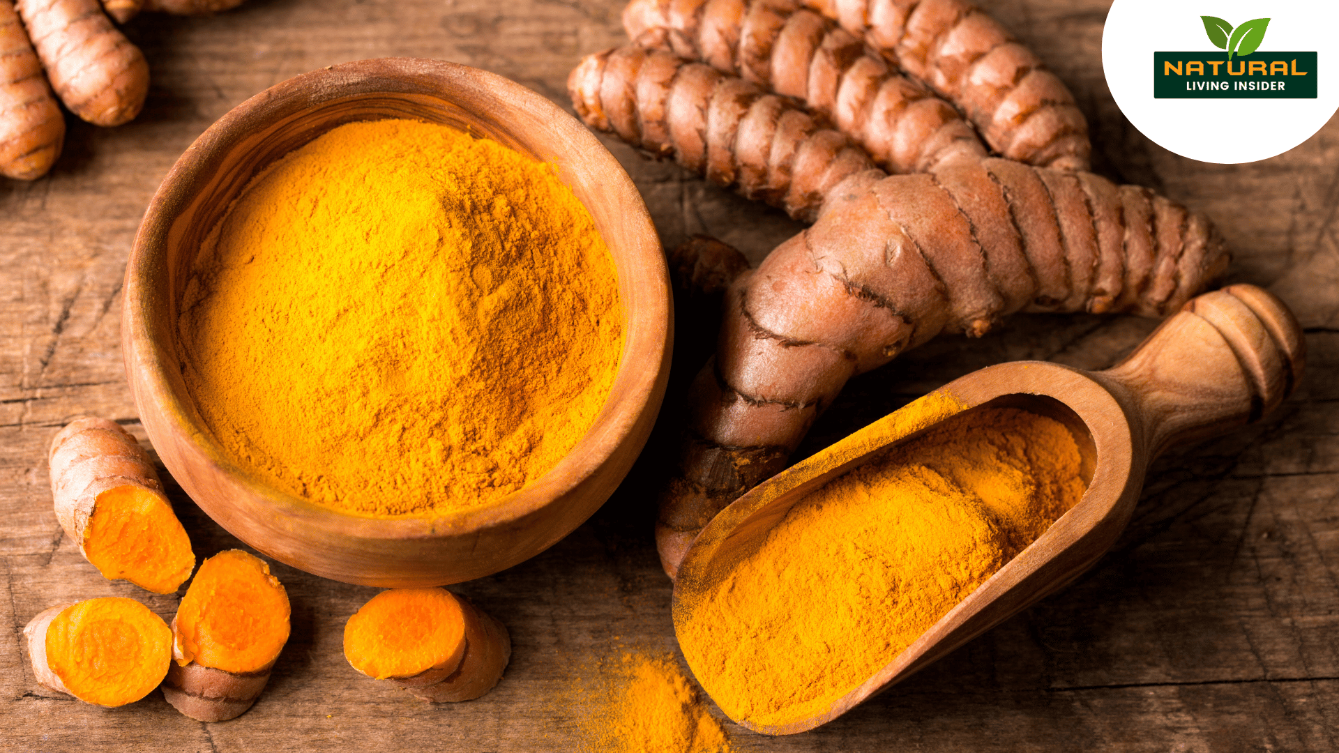 A bowl of bright yellow turmeric powder beside whole turmeric roots and a wooden scoop on a rustic wooden surface.
